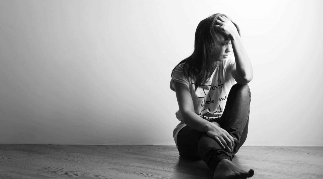 Teenager girl with depression sitting alone on the floor in the dark room. Black and white photography